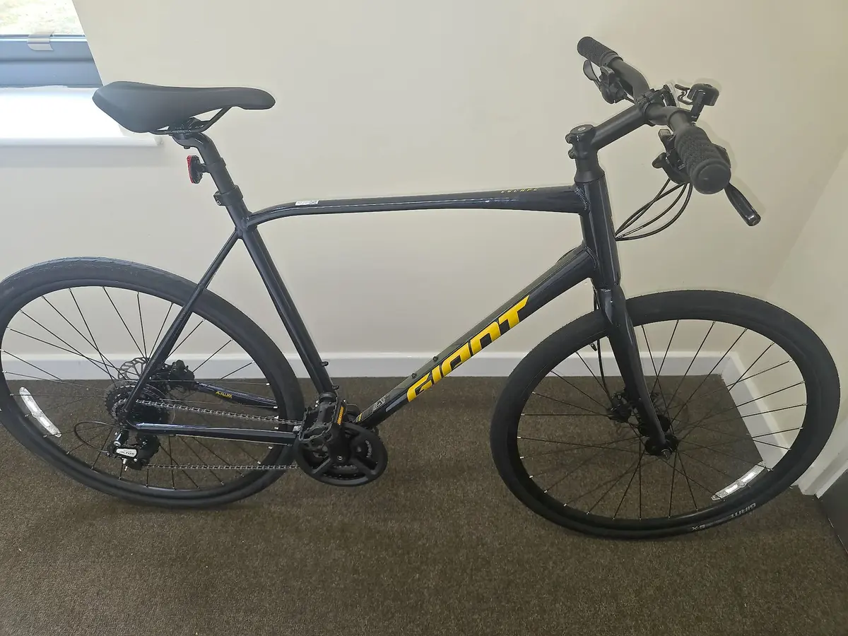Black and yellow Giant hybrid bike on carpet indoors, drive side, against a white wall with window.