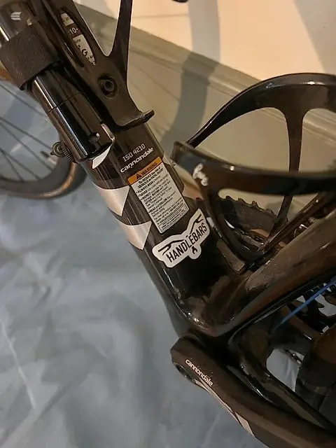 Close-up of black bicycle handlebars and stem with brake lever visible, alongside black-framed sunglasses on a light grey surface indoors.