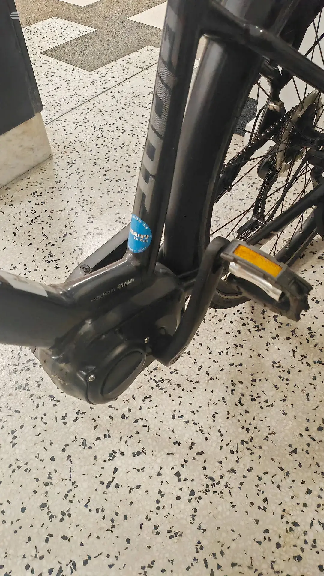 Black Yamaha e-bike front wheel and fork close-up, non-drive side, on speckled concrete floor indoors.