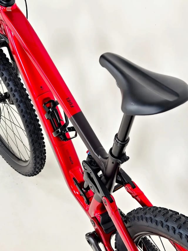 Red hardtail mountain bike with black saddle and components, shot from the drive side at a 45-degree angle against a white background.