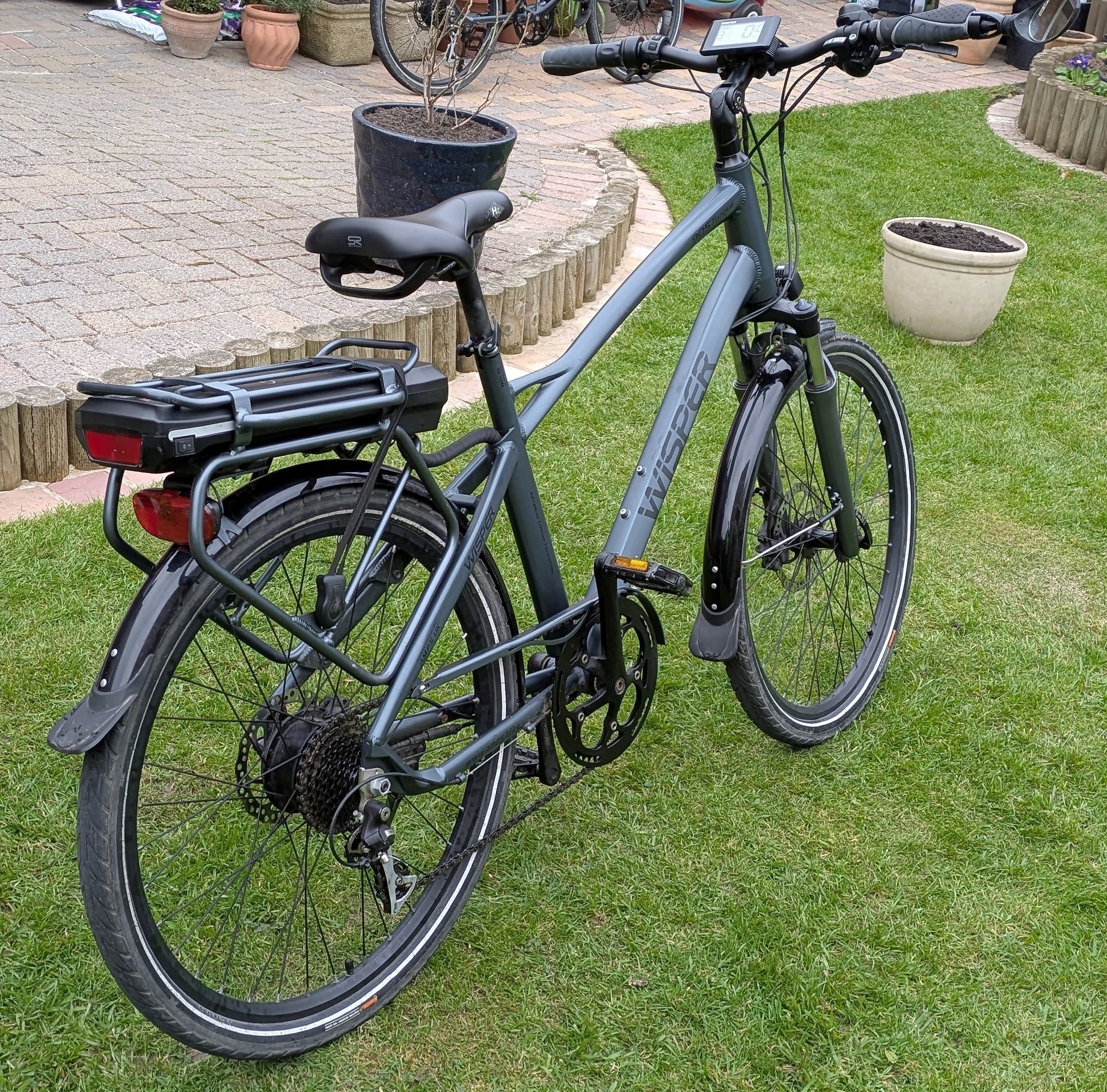 Blue-grey electric cargo bike with rear battery pack and mudguards, parked on grass, drive side view, residential garden setting.