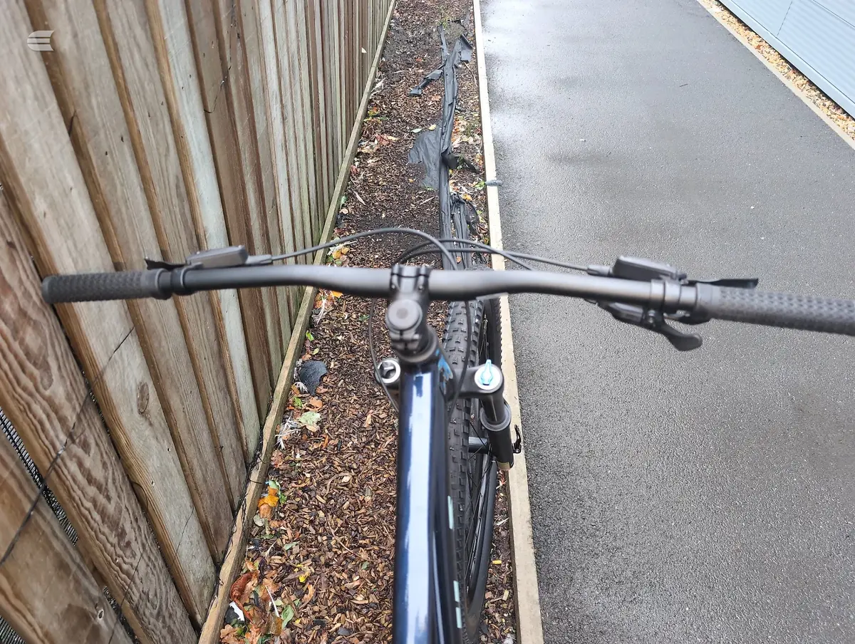 Blue mountain bike on asphalt driveway, front-on view, parked between wooden fence and concrete path.