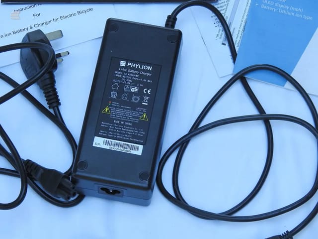 Phylion lithium battery charger for electric bicycle with instruction manual and power cable on blue background.