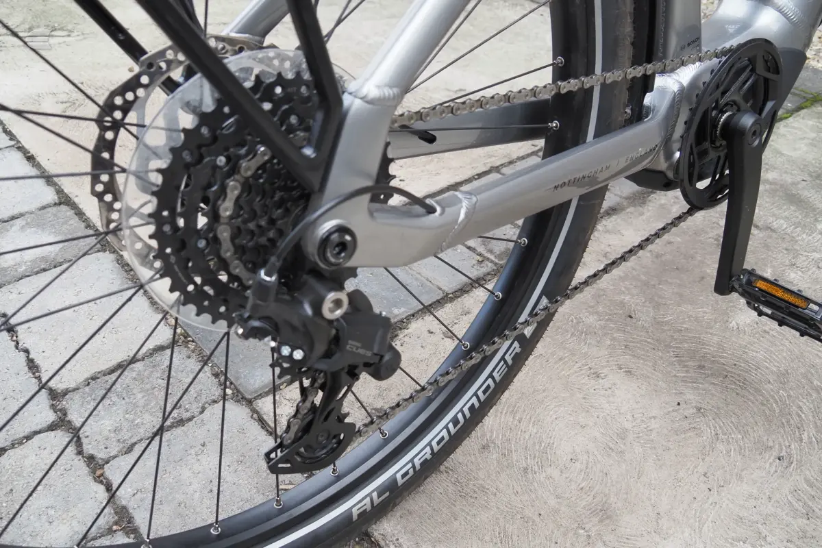 Silver Marin mountain bike, rear drivetrain close-up showing cassette, chain, and derailleur on concrete ground, drive side.