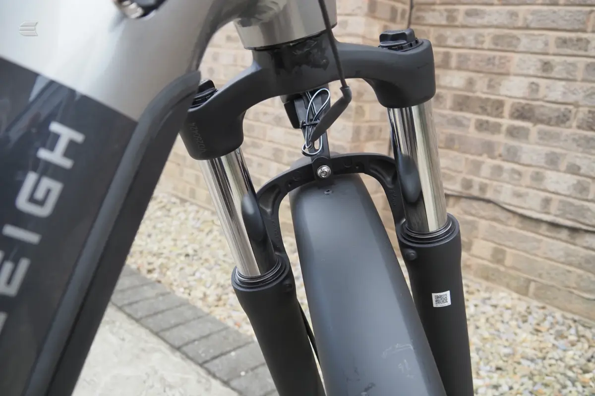 Close-up of front fork and headtube on black and grey hardtail mountain bike, non-drive side, against brick wall background.