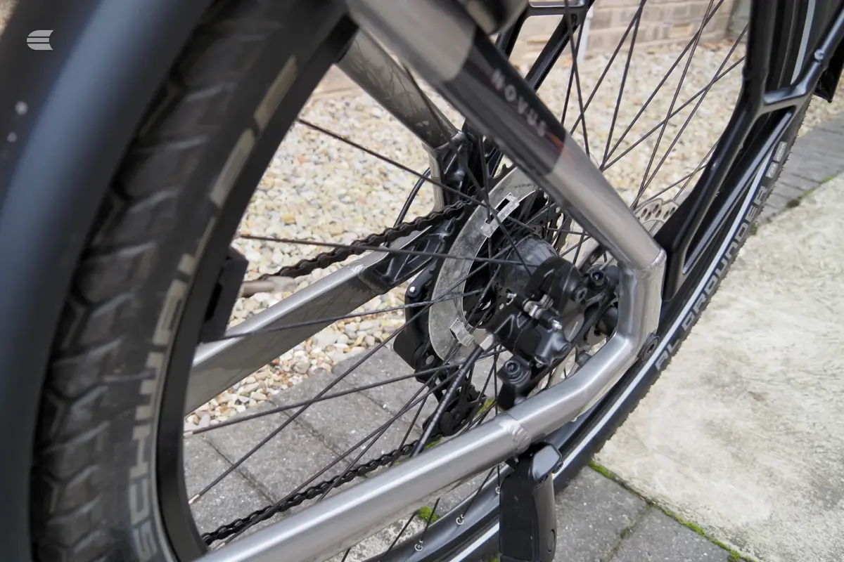 Close-up of rear hub, cassette and derailleur on a black bike, drive side, on pavement with gravel background.