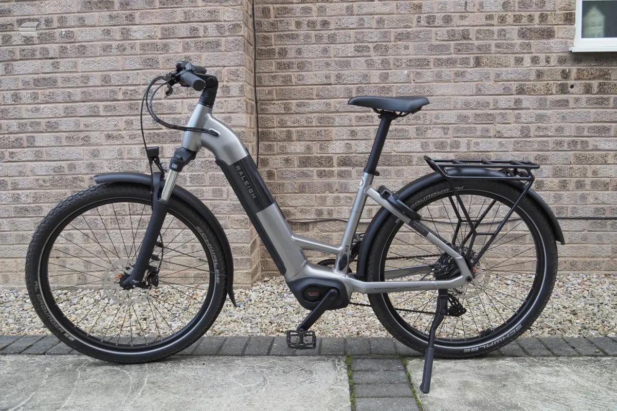 Silver and black Riese & Müller electric cargo bike on kickstand, non-drive side, against brick wall.