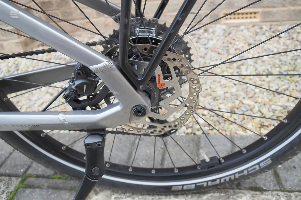 Close-up of front wheel and disc brake on silver and black hybrid bike, drive side, on gravel ground.