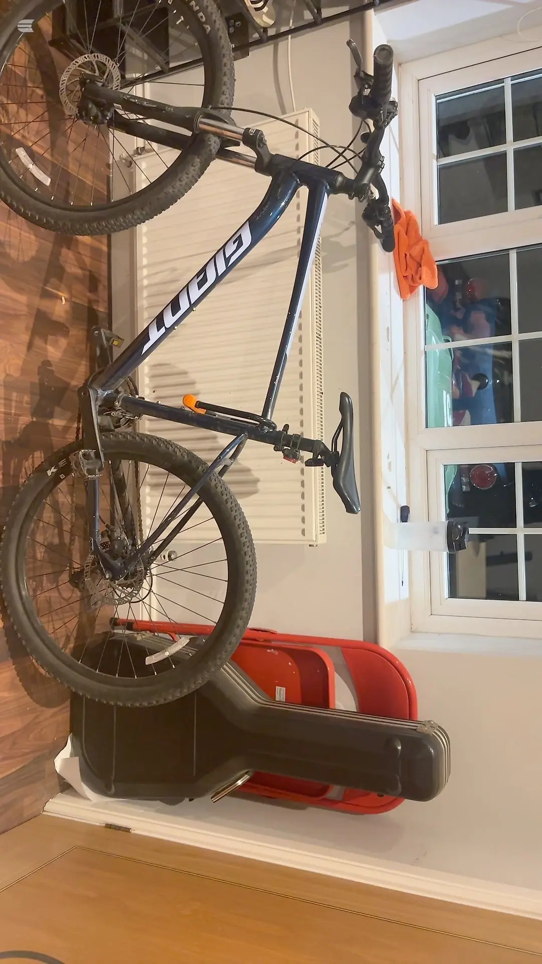 Blue and white Sworks mountain bike on a red and black floor stand, non-drive side, indoors against a white door and siding.