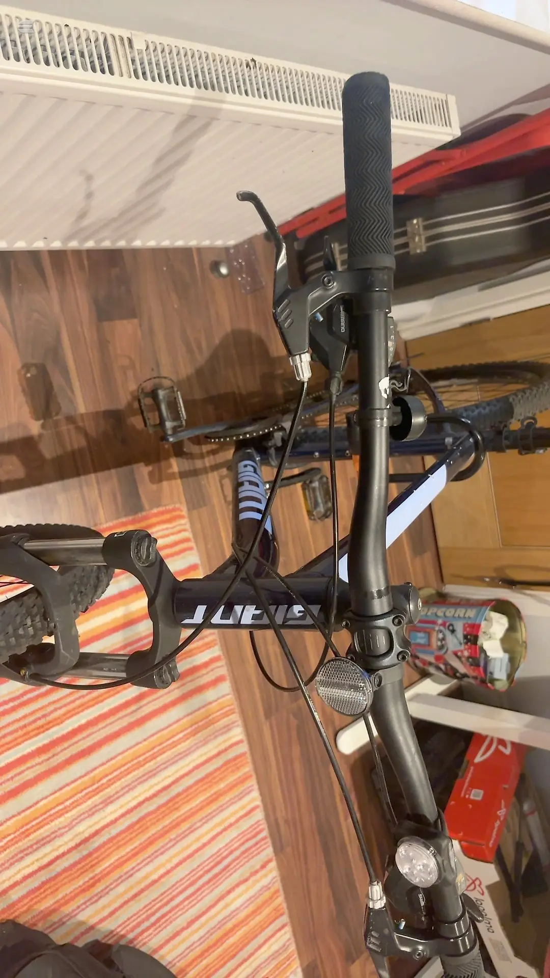Black hardtail mountain bike on a stand, drive side, indoors against striped fabric and metal shelving.