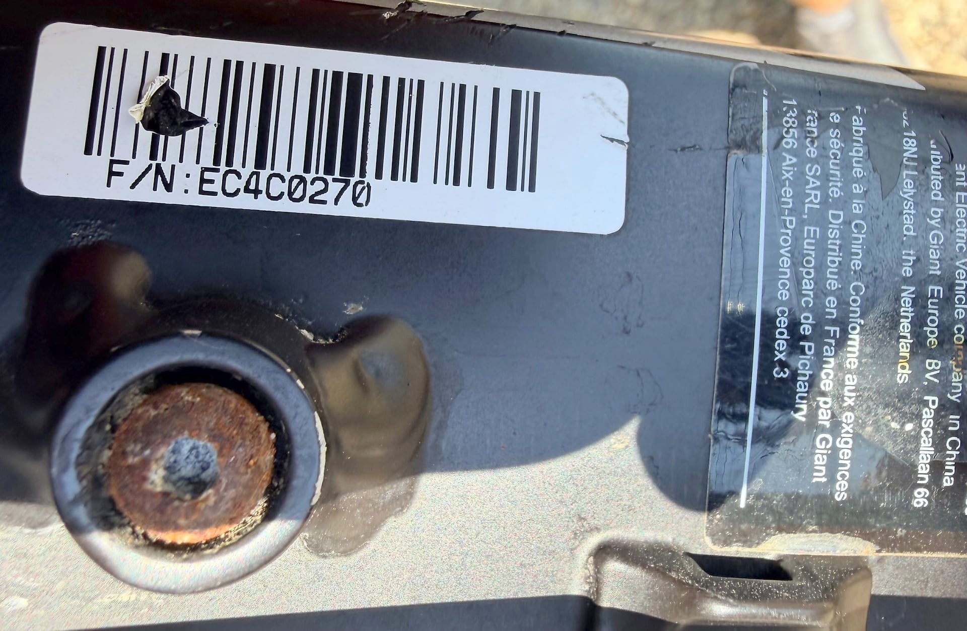 Barcode label and product information label on a dark cylindrical object, close-up overhead view.