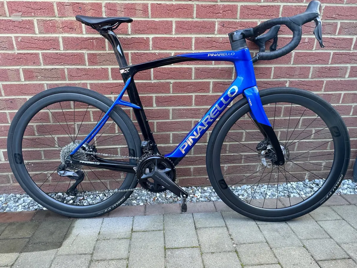 Blue and black Pinarello road bike with disc brakes, drive side, leaning against a red brick wall with white gravel at the base.