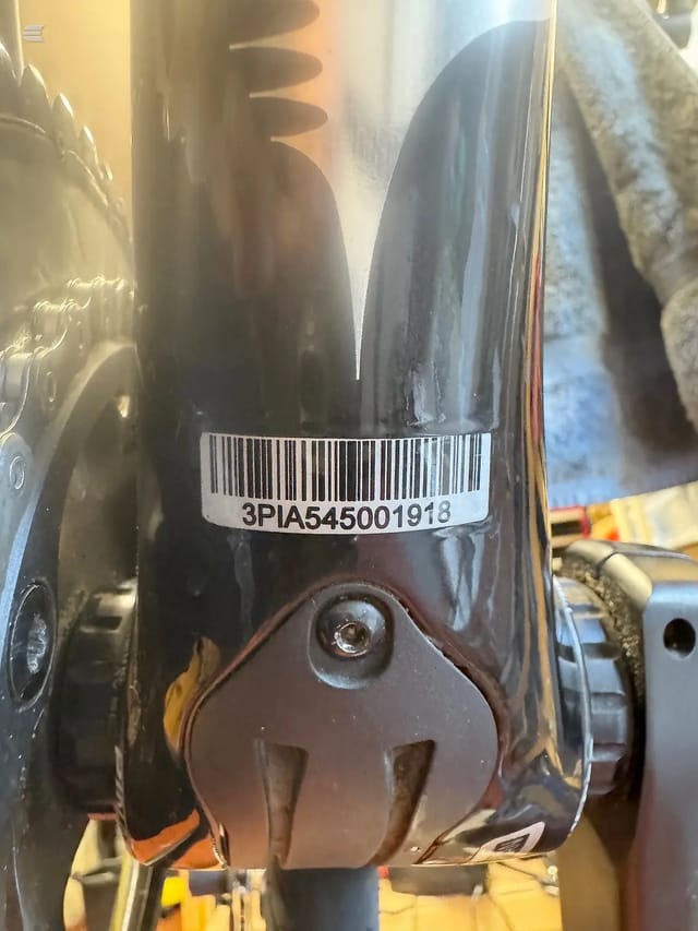 Close-up of a black bicycle rear hub and dropout area, showing a barcode label affixed to the seat tube, mounted on a yellow work stand.