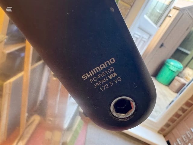 Close-up of Shimano FC-R8100 crankset component showing model number and Japan origin marking on black housing.