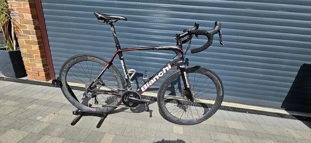 Black and red Bianchi road bike on a stand, drive side, against a blue metal shutter and brick wall.