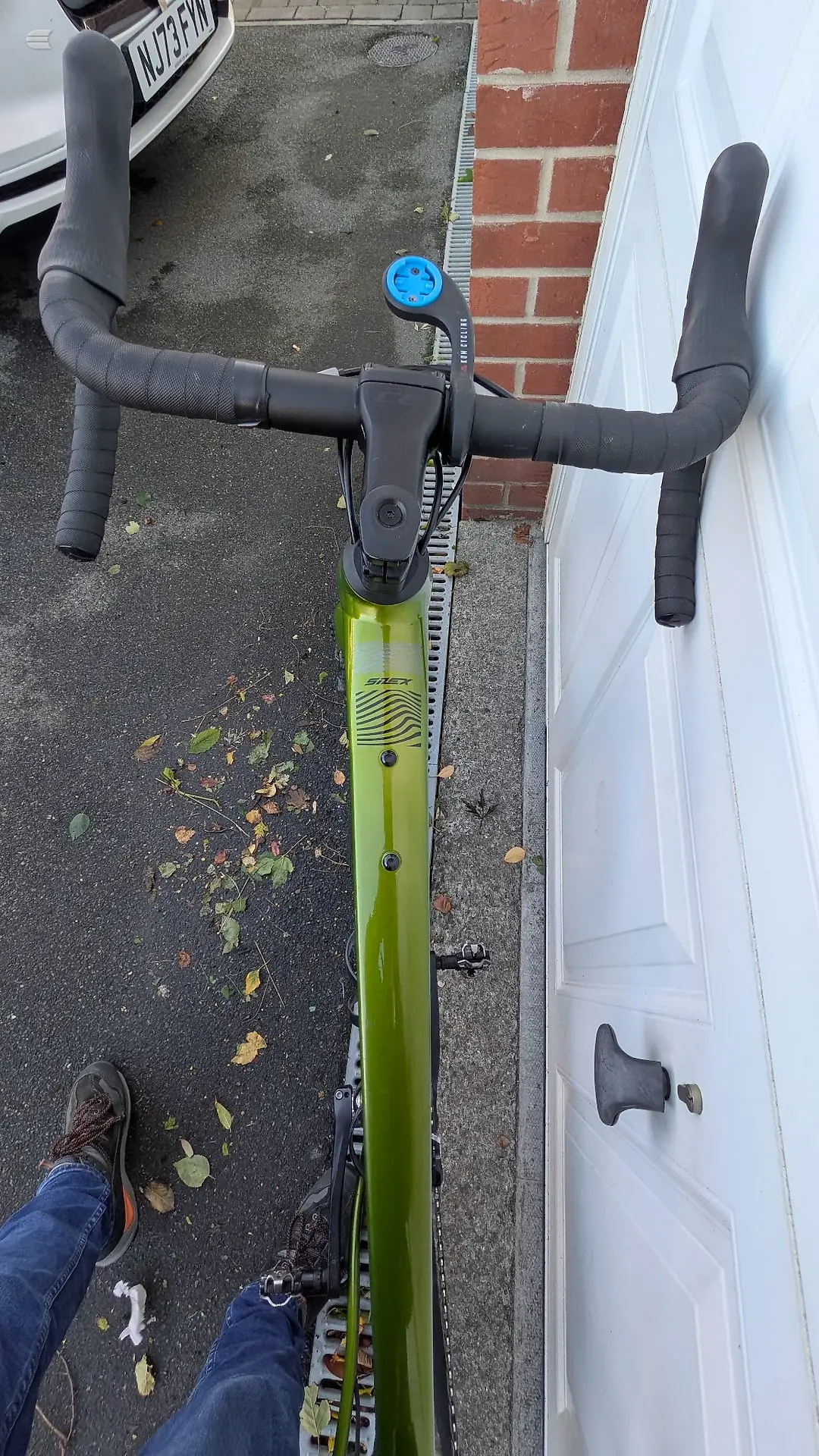 Lime-green gravel or hybrid bike with drop bars, viewed from above on a driveway, drive side, parked against a brick wall and white garage door.