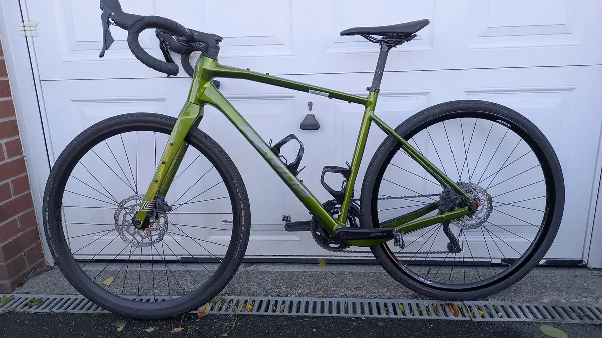 Lime-green gravel bike with disc brakes, drop bars, and black saddle, photographed side-on against a white garage door, drive side visible.