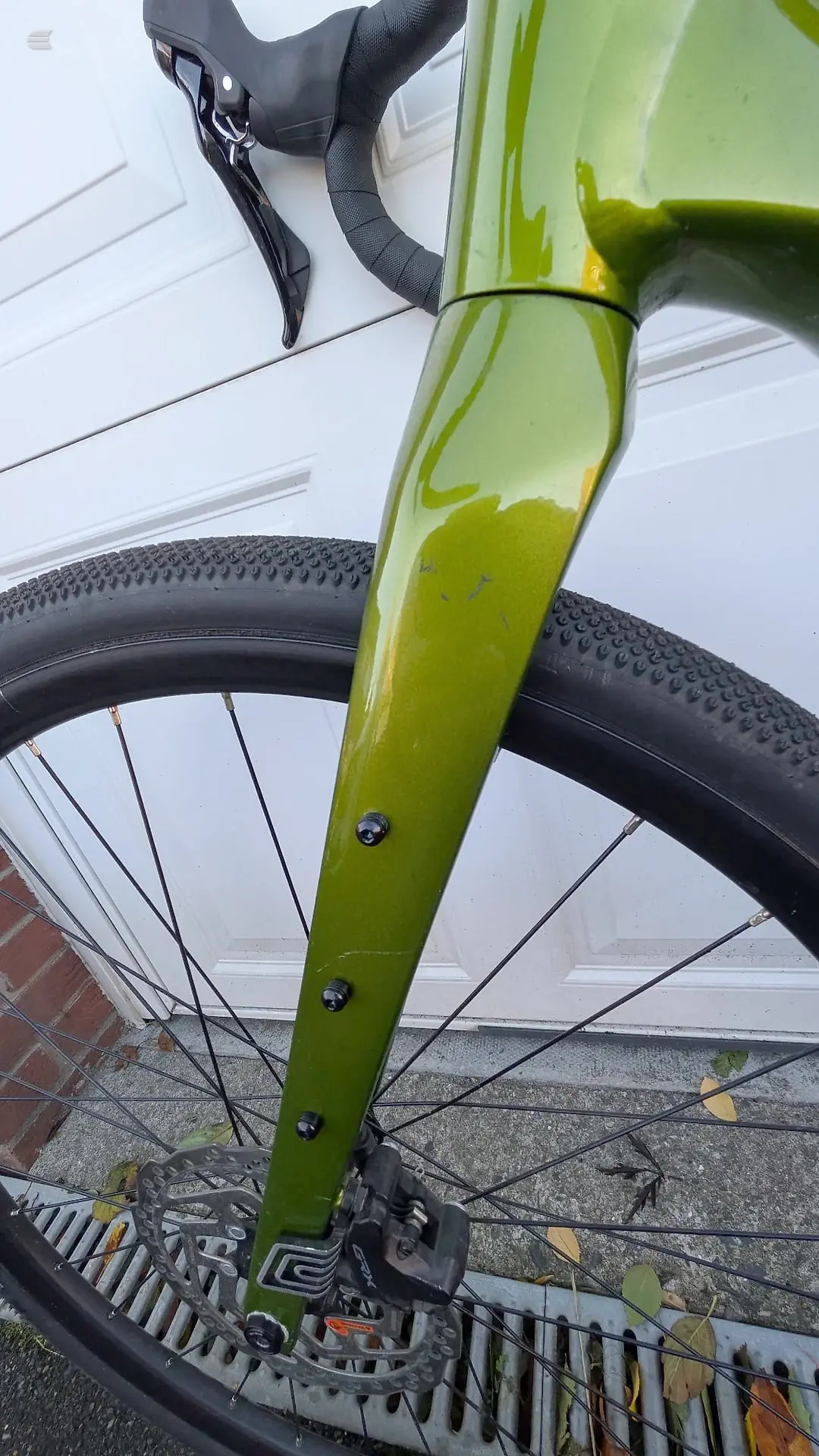 Lime-green gravel bike frame, non-drive side, leaning against white garage door with black wheel and drivetrain visible.