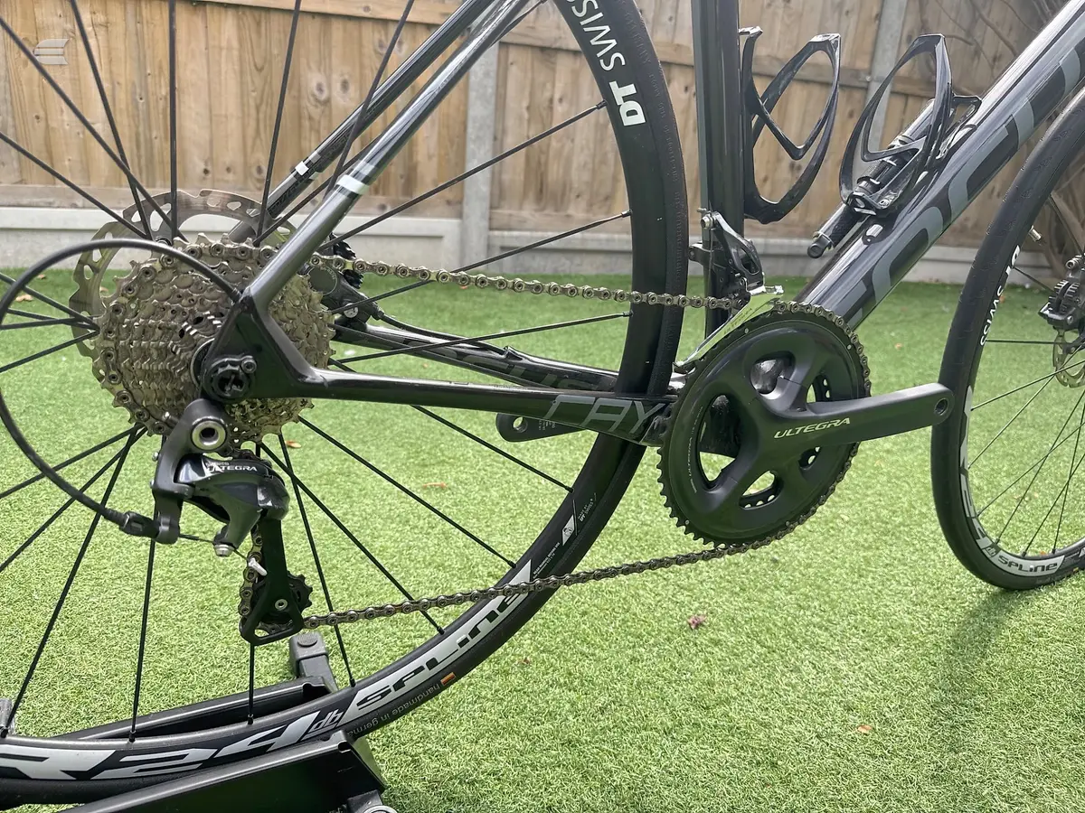 Shimano Ultegra drivetrain on a black road bike, drive side close-up showing crankset, chain, and rear derailleur on artificial grass.