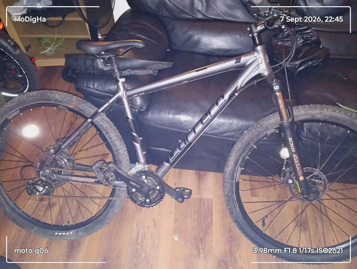 Silver gravel bike with disc brakes on wooden floor, drive side, indoors with dark leather seating visible above.