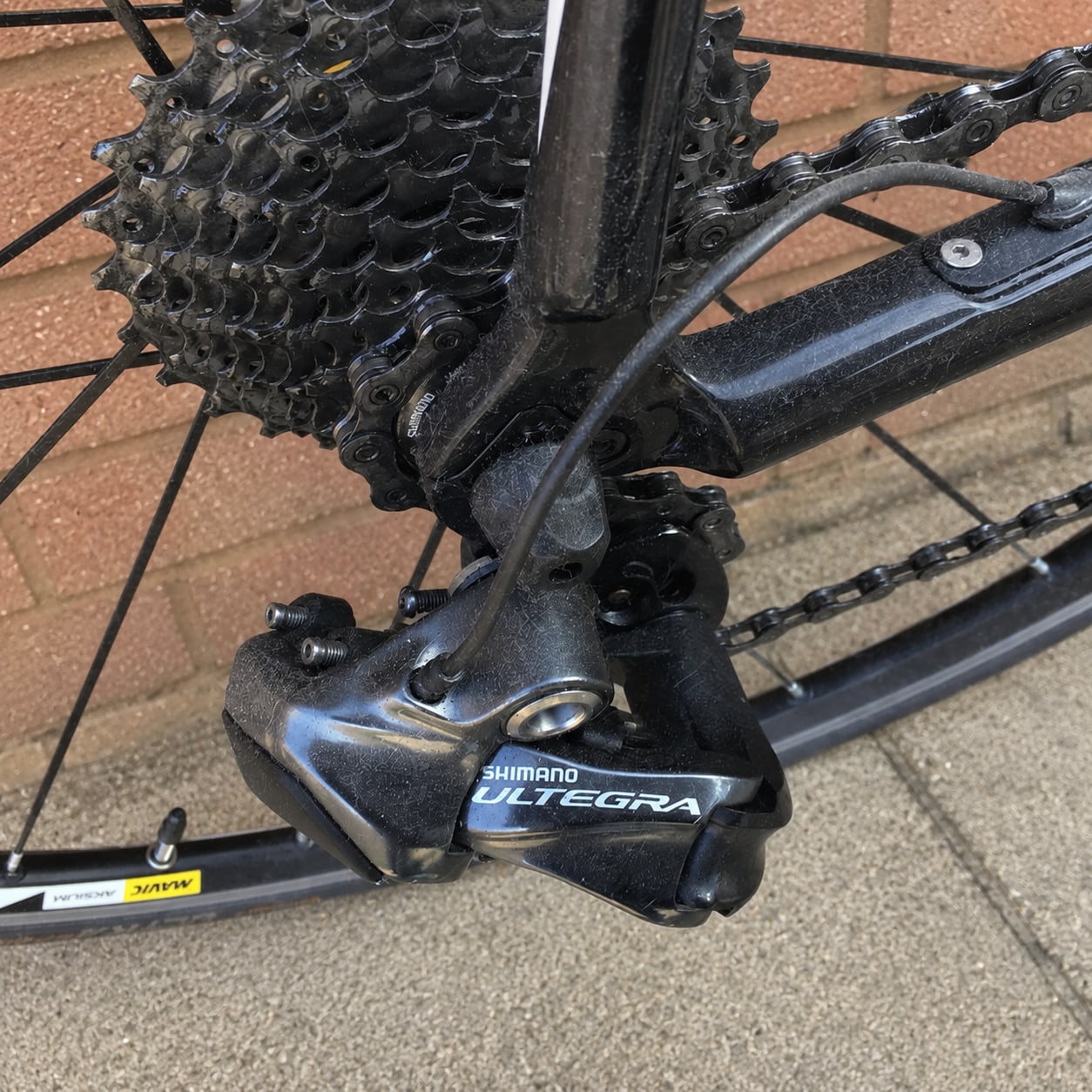 Shimano Ultegra rear derailleur and cassette on black road bike, drive side close-up, outdoor setting on pavement.