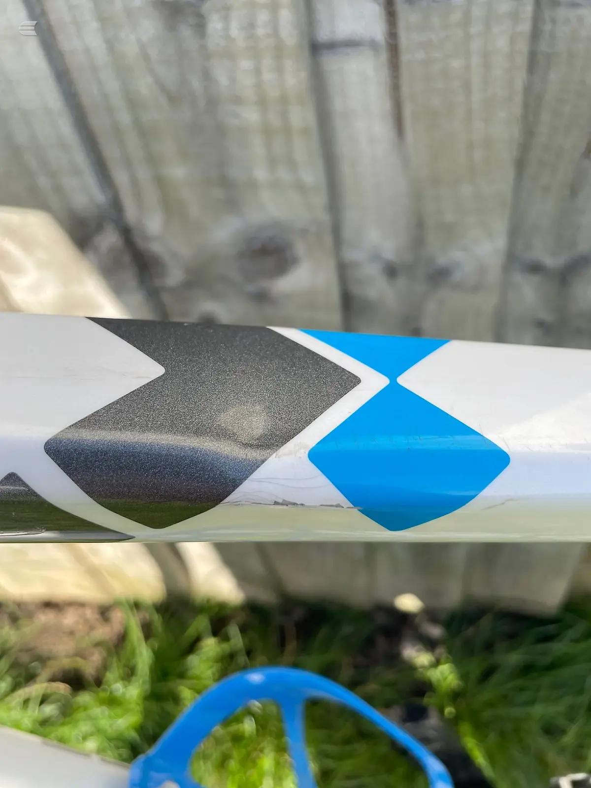 Close-up of a white and blue bicycle frame tube with geometric logo decals, on grass with blurred background.