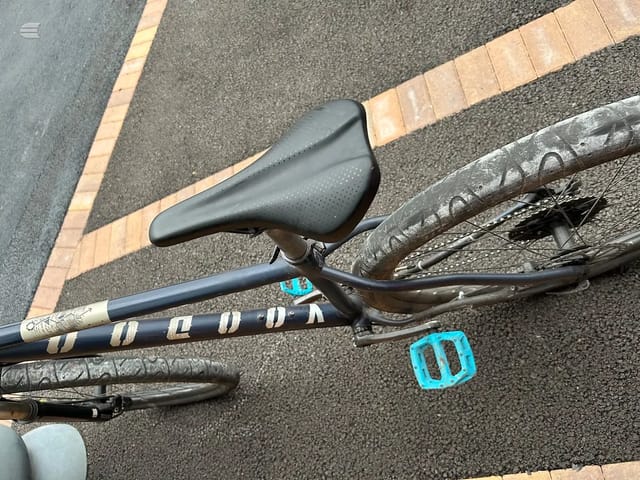 Black drop-bar road bike saddle and stem detail, overhead view on asphalt with brick edging.