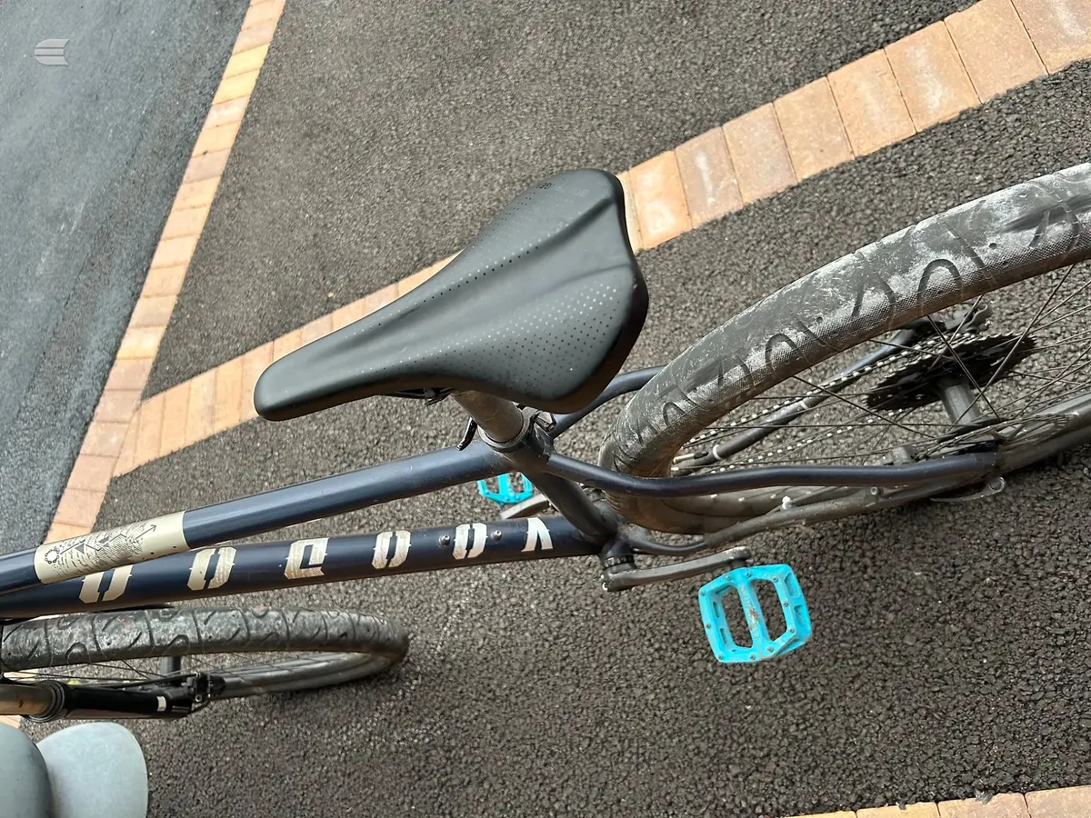 Black drop-bar road bike saddle and stem detail, overhead view on asphalt with brick edging.