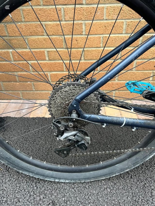 Close-up of bicycle rear derailleur, cassette and chain against brick wall background, drive side view.