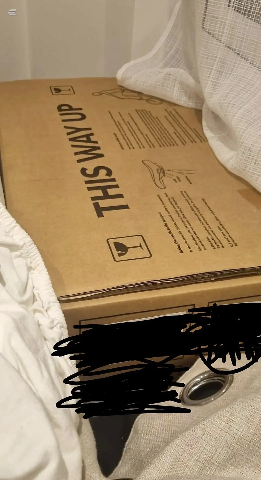 Cardboard shipping box with 'THIS WAY UP' text and fragile handling symbols, white mesh netting visible, black marker scribbles on contents.