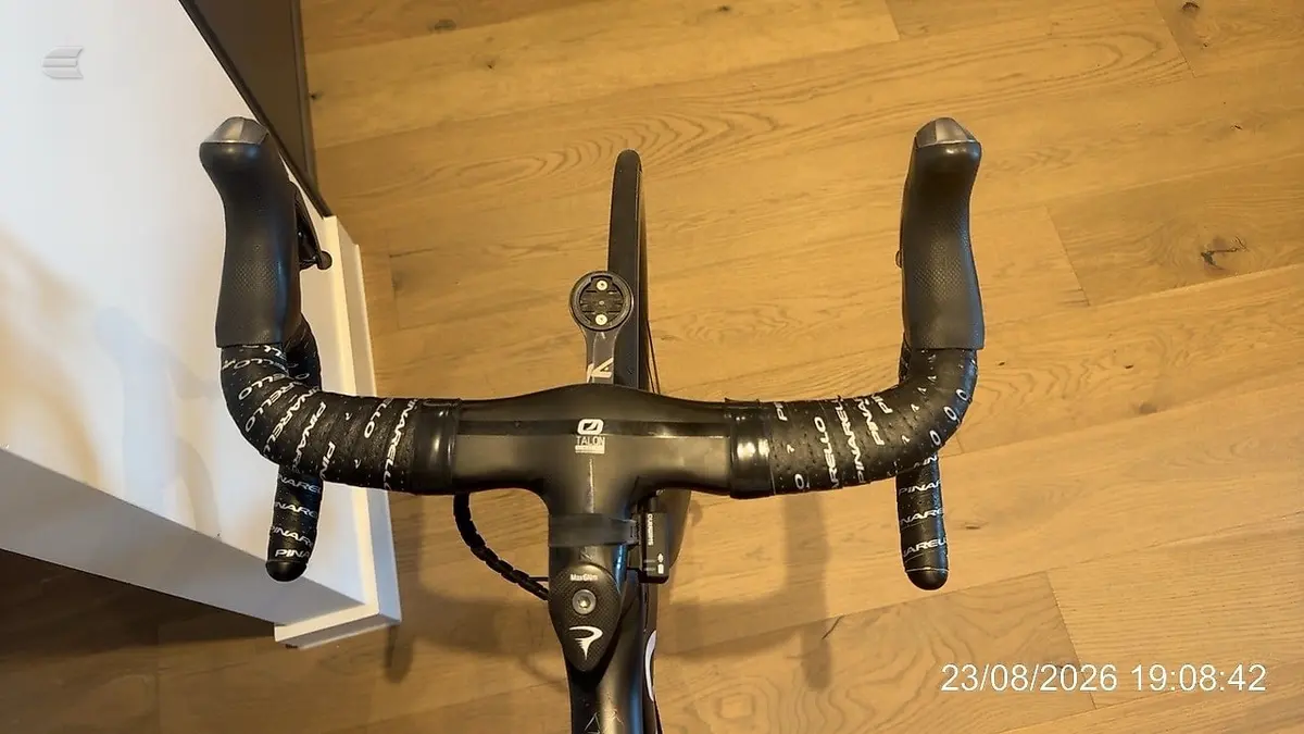 Black drop-bar road bike on wooden floor, front-on view, handlebars and both wheels fully visible.