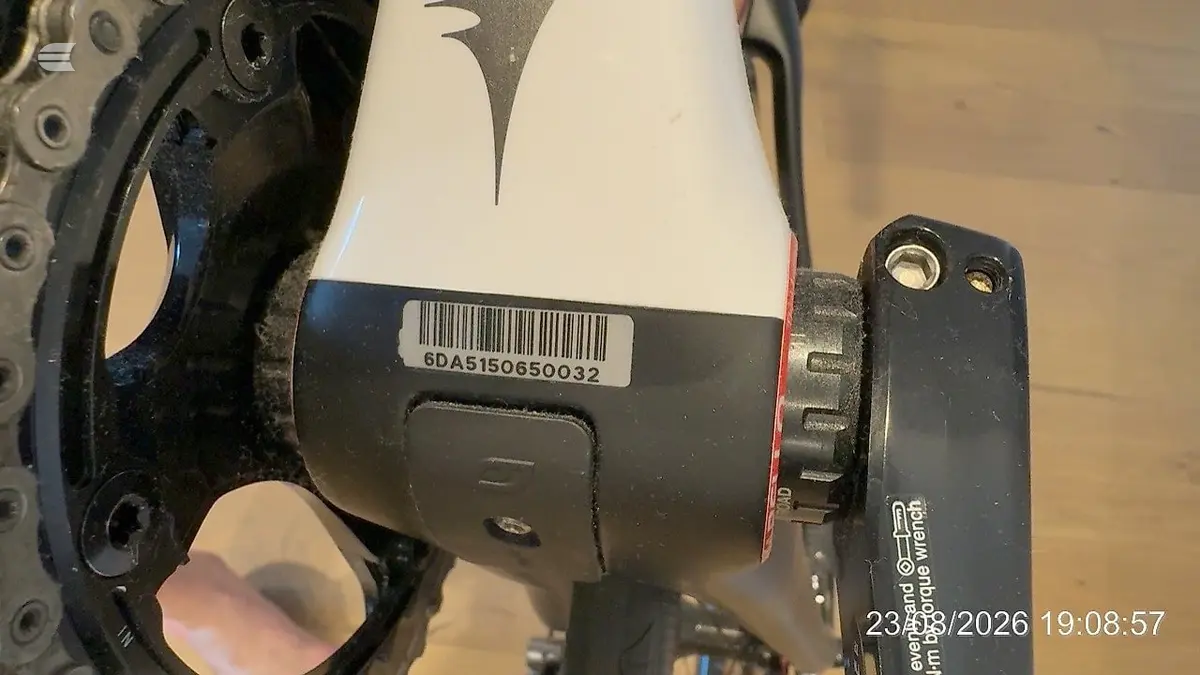 Close-up of bicycle disc brake caliper and rotor, black metal components on wooden floor, angled view showing mechanical detail.