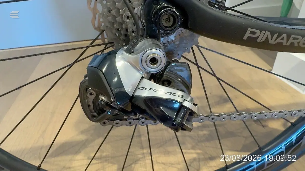 Shimano Dura-Ace rear derailleur on blue Pinarello road bike, drive side close-up, wooden floor background.