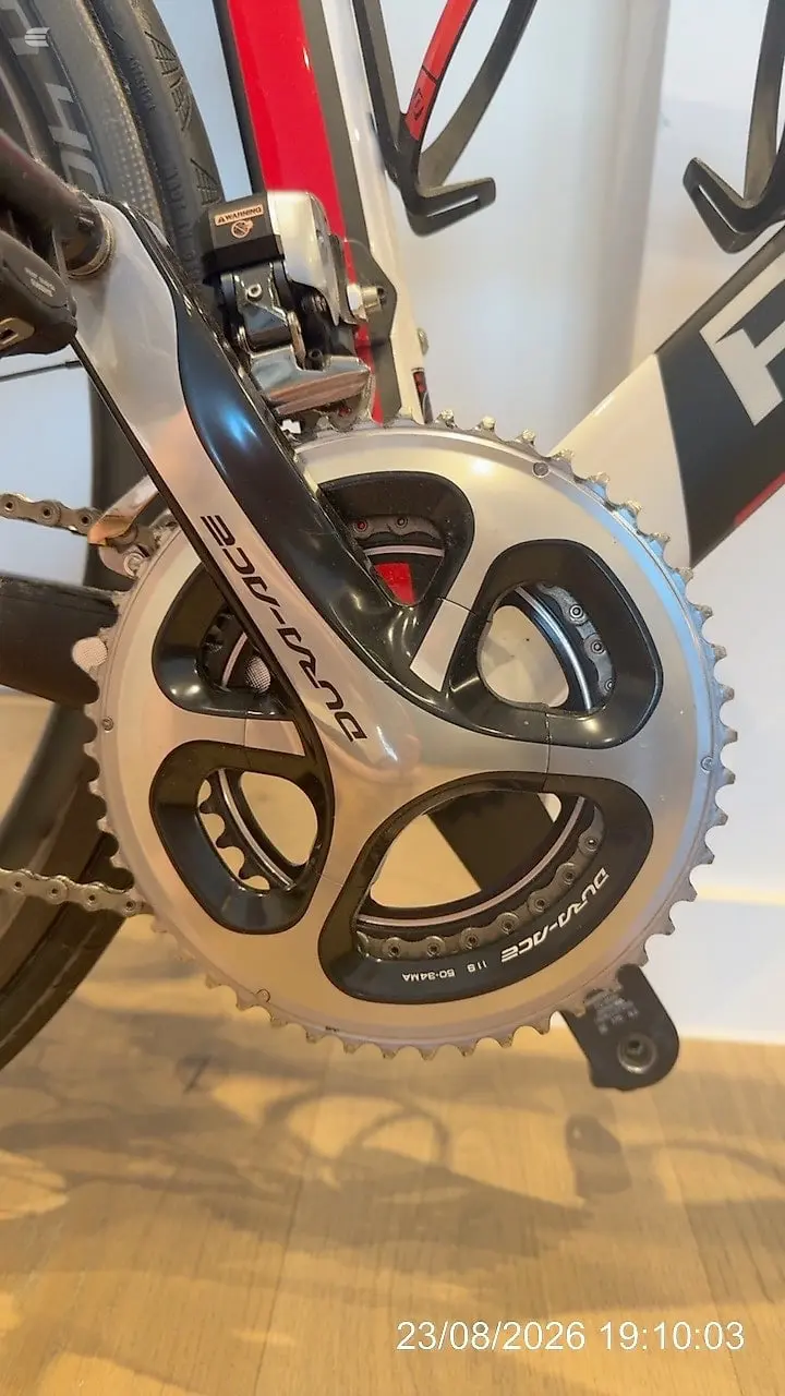 Shimano Dura-Ace crankset with white and black chainrings on a road bike, drive side, indoors on wooden floor.