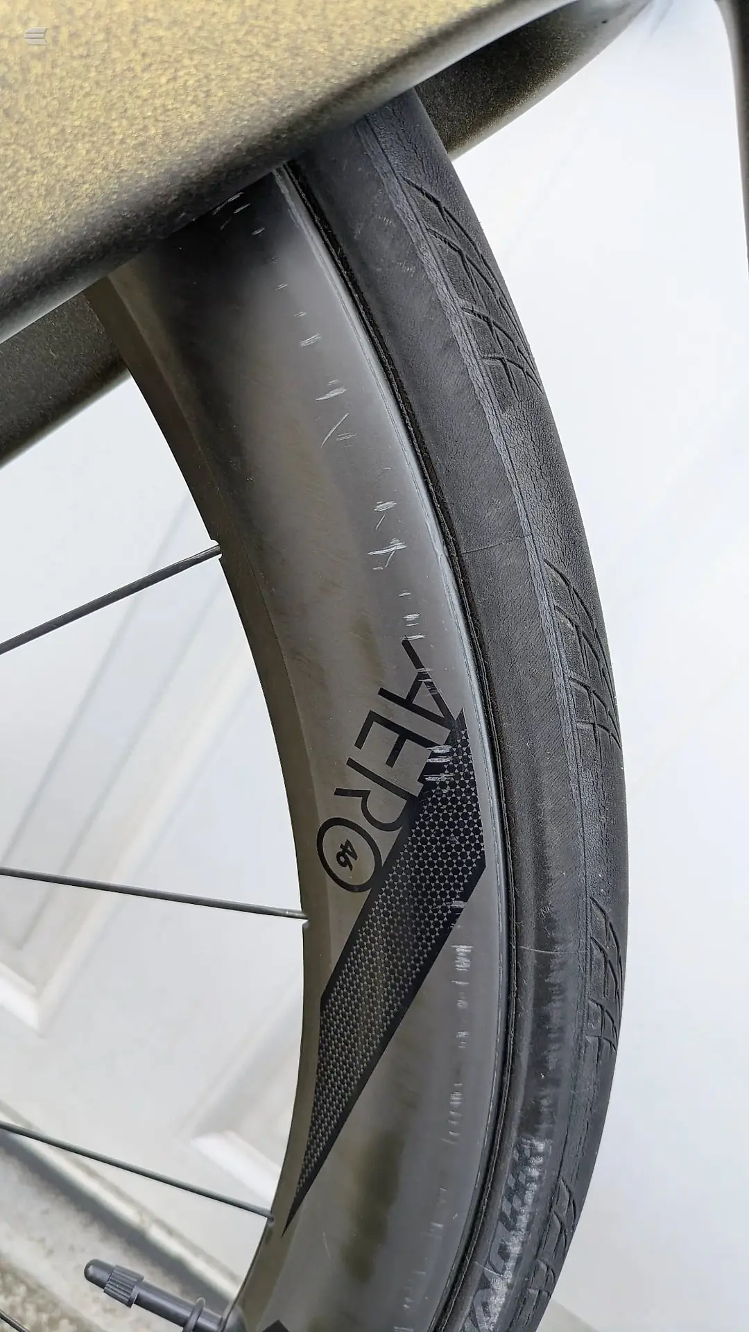 Close-up of a bicycle wheel rim and tyre, non-drive side, showing carbon fibre rim with brand decal and black tyre tread against a white background.