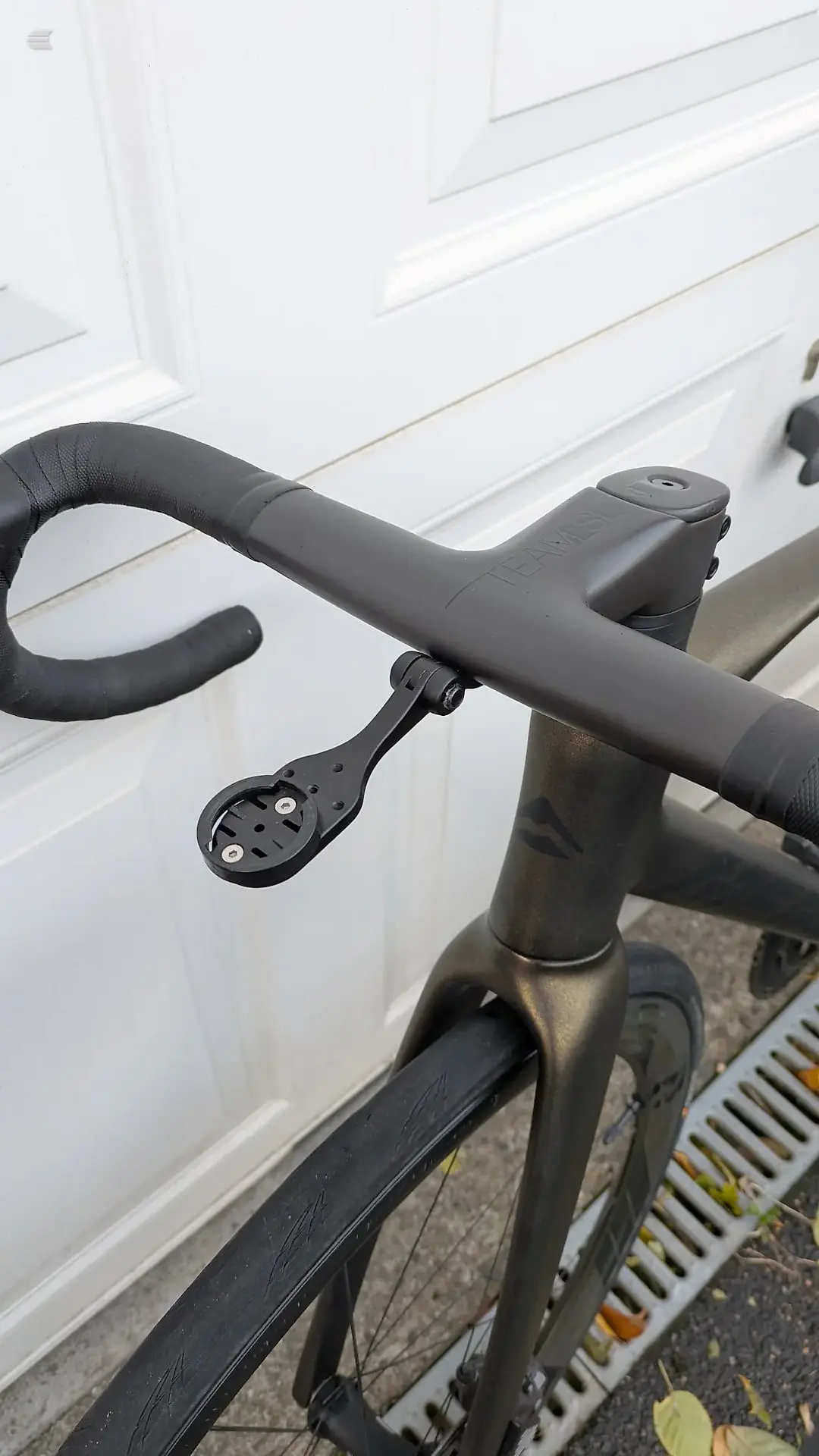 Black drop-bar road bike handlebars and stem, non-drive side, against a white garage door.