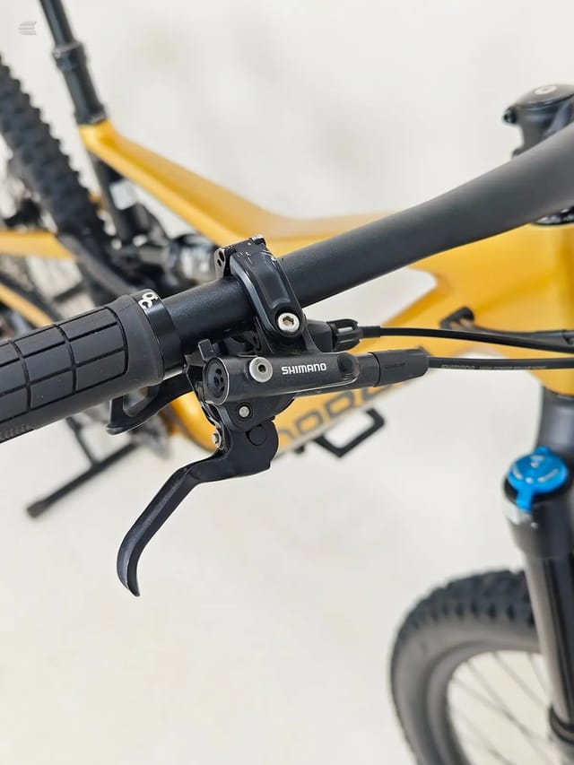 Shimano hydraulic disc brake lever and caliper on yellow mountain bike handlebar, close-up detail shot.