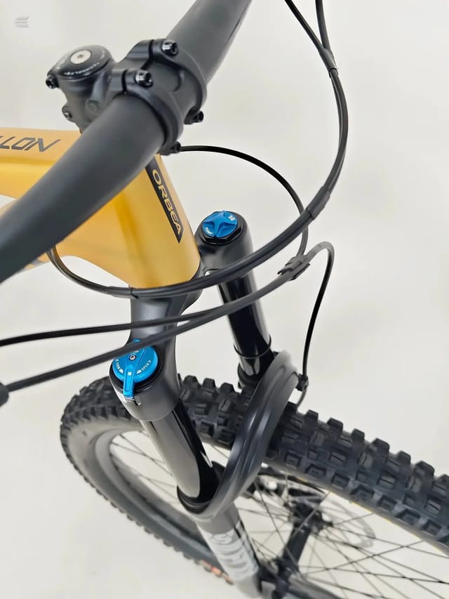 Yellow Orbea gravel bike, front end detail showing hydraulic disc brake lever and stem with headset adjustment, non-drive side, against white background.