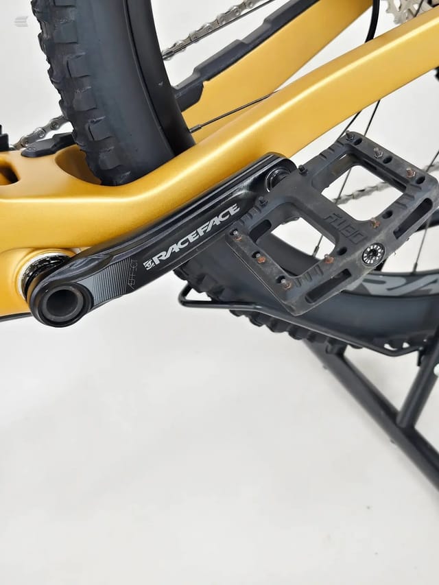 Yellow hardtail mountain bike, drive-side view of crank and pedal area with Raceface crank arm and flat pedal, against white background.