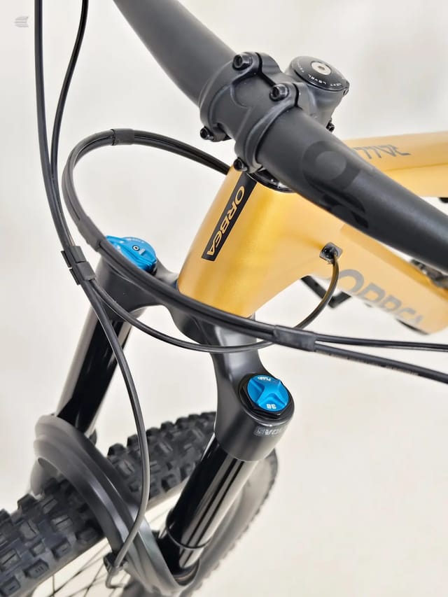Yellow hardtail mountain bike, close-up of handlebar stem and brake lever assembly with blue adjustment dials, non-drive side, against white background.