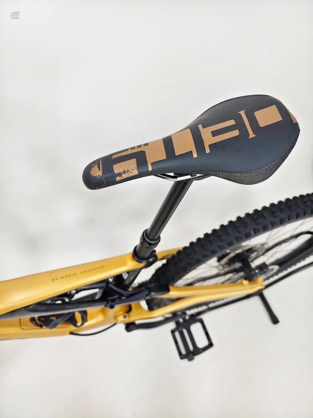 Black and tan saddle with 'ALIBI' branding on yellow hardtail mountain bike, close-up detail shot against white background.
