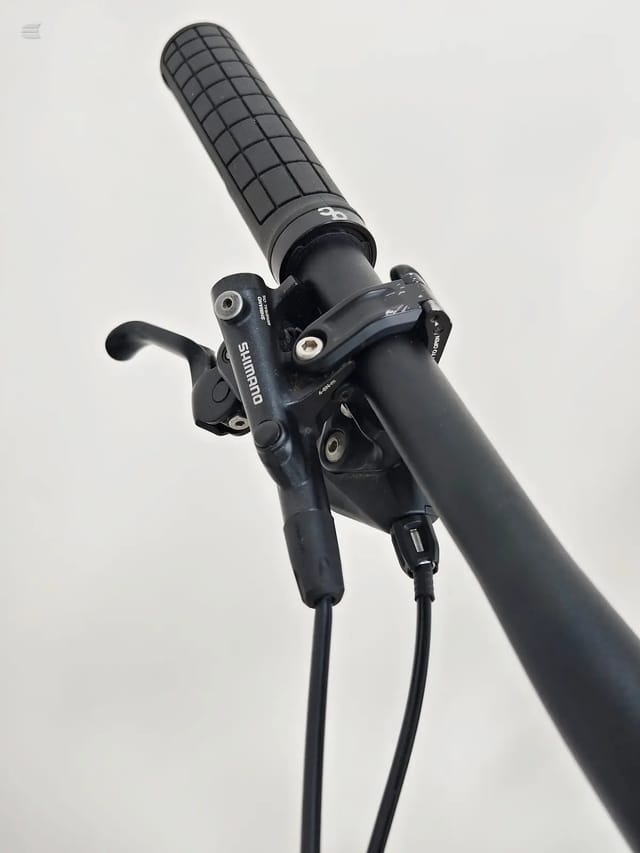 Shimano brake lever and grip on black bicycle handlebar, angled upward against white background.