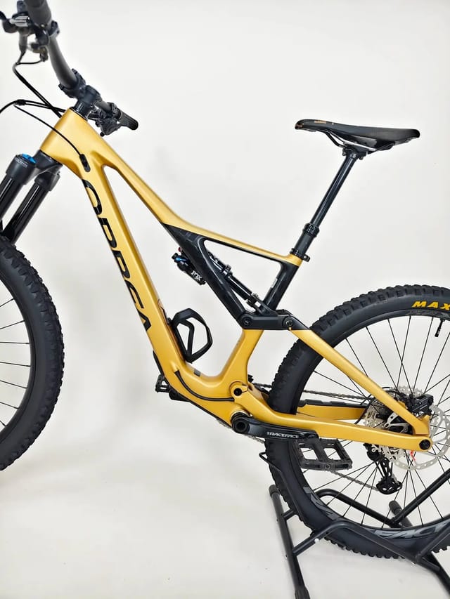 Gold and black full-suspension mountain bike on a stand, drive side, against a white background.