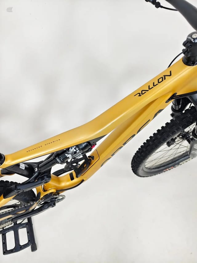 Yellow Nolloy hardtail mountain bike, drive side, angled upward against overcast sky with black pedals and tyres visible.