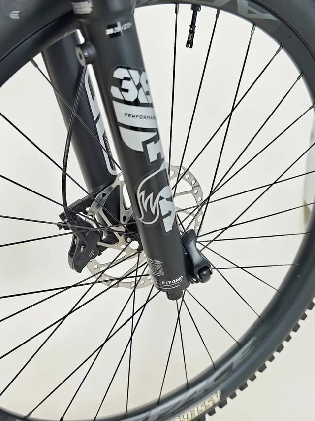 Close-up of front wheel and fork on black performance mountain bike, non-drive side, against white background.