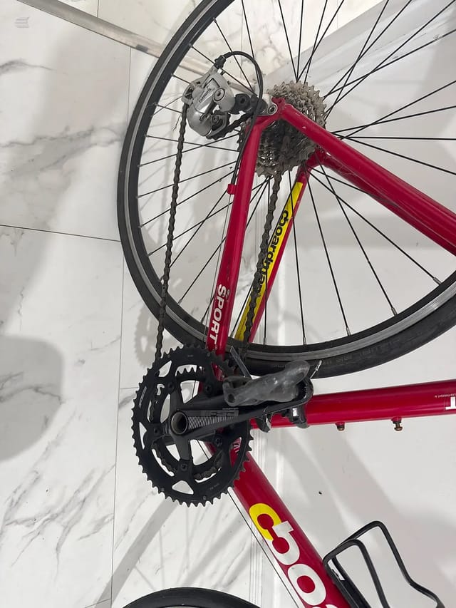 Red sport bike rear drivetrain and cassette, close-up of chain, derailleur, and sprockets against marble background, drive side.