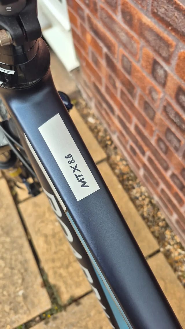Close-up of MTX 8.8 bicycle frame tube with white label against red brick wall, daytime outdoor setting.