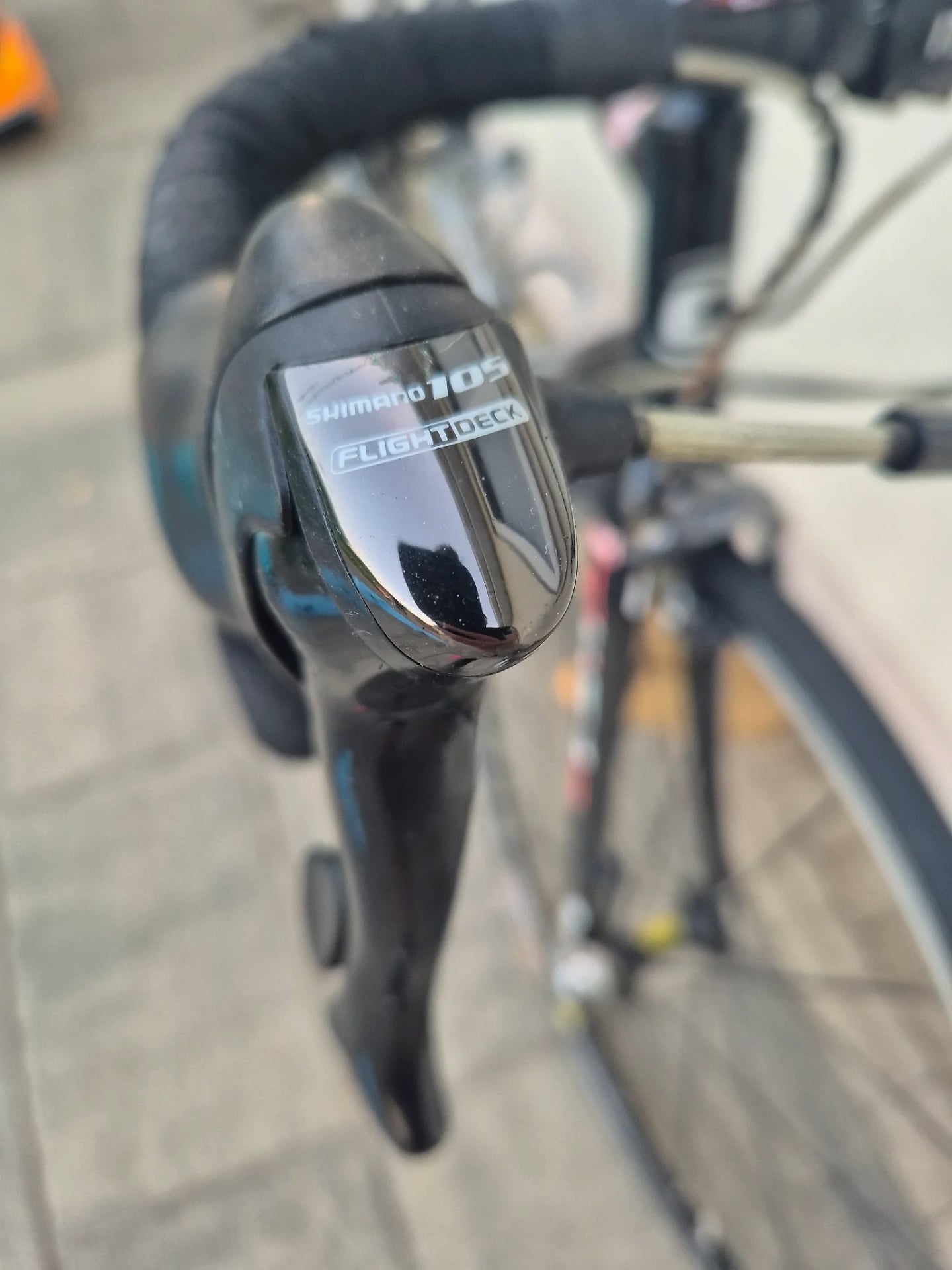 Shimano 105 Flight Deck shifter on black drop bar, close-up detail shot on pavement.