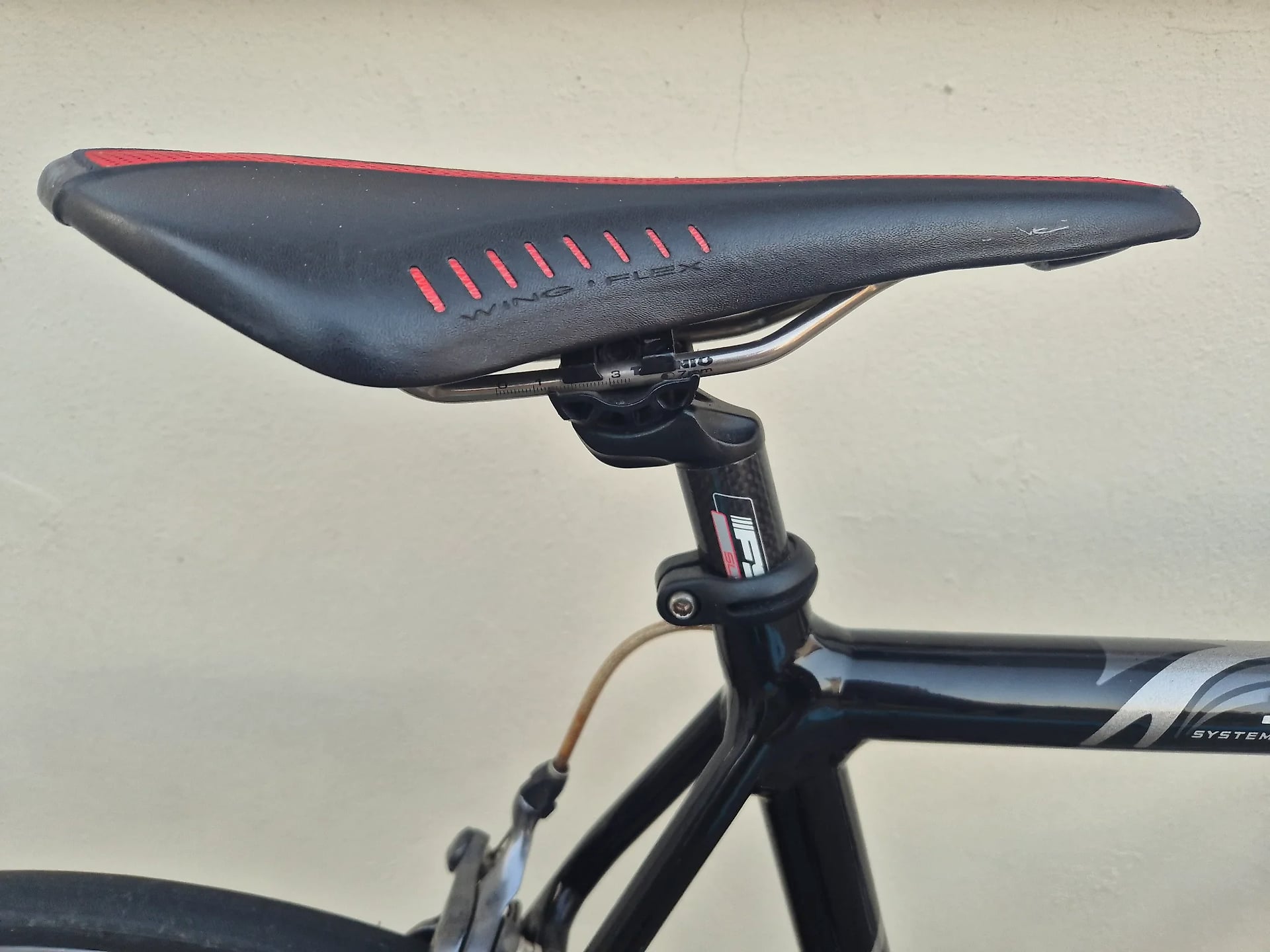 Black and red bicycle saddle with ventilation slots, mounted on seatpost, against neutral background. Non-drive side view.
