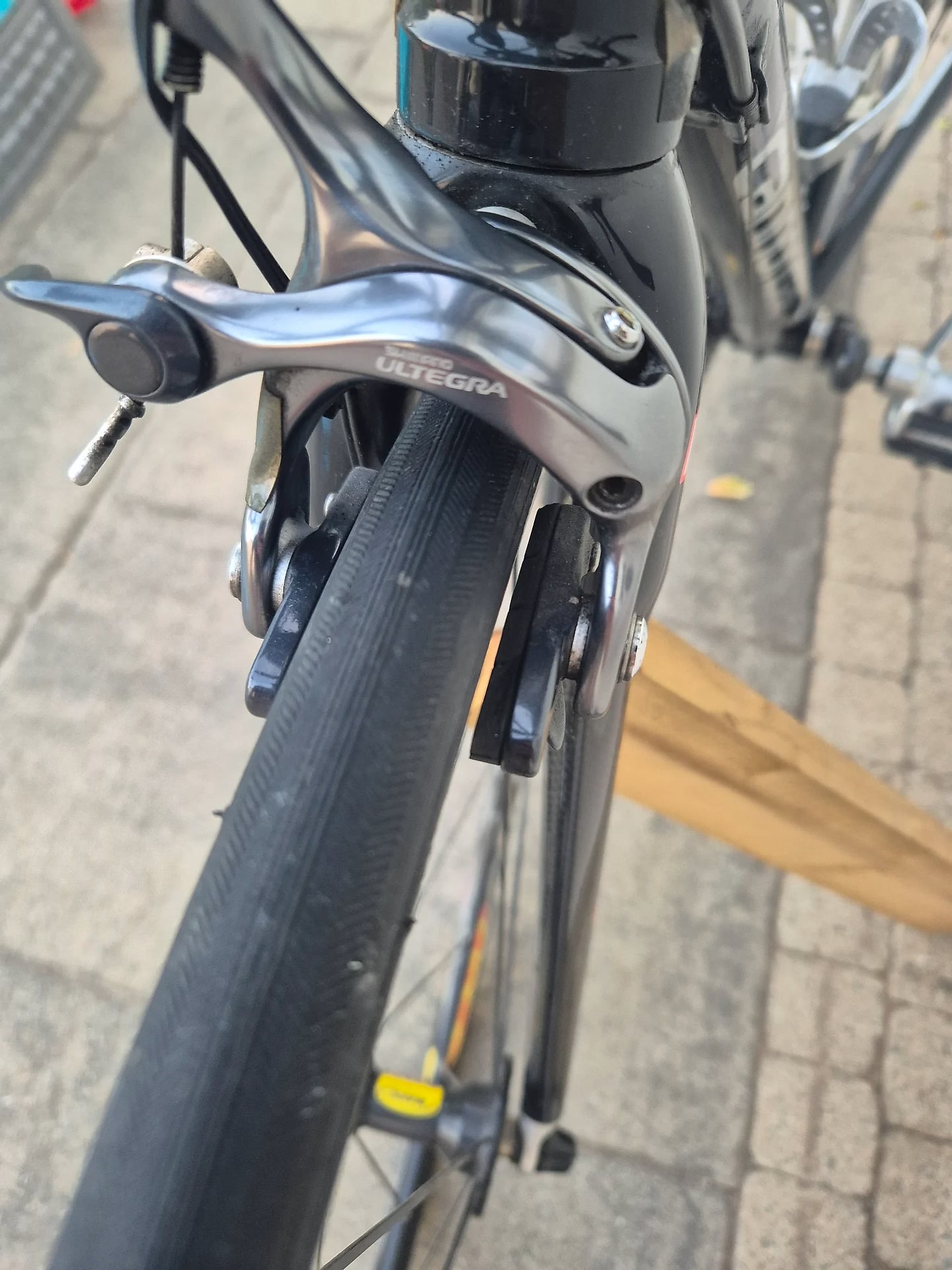 Shimano Ultegra brake caliper and lever on a road bike, close-up of the front brake assembly, drive side view on pavement.